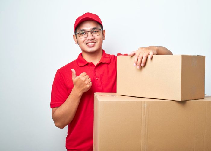 confident-asian-courier-red-uniformencourage-call-service-show-thumbup-lean-cardboard-boxes